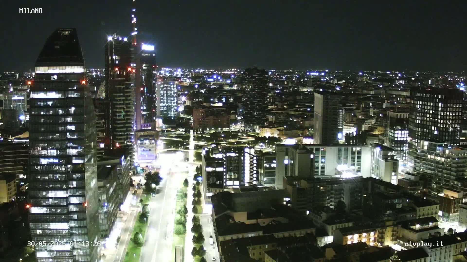 A nighttime aerial view of a city with many illuminated buildings and streets, showing a clear sky.