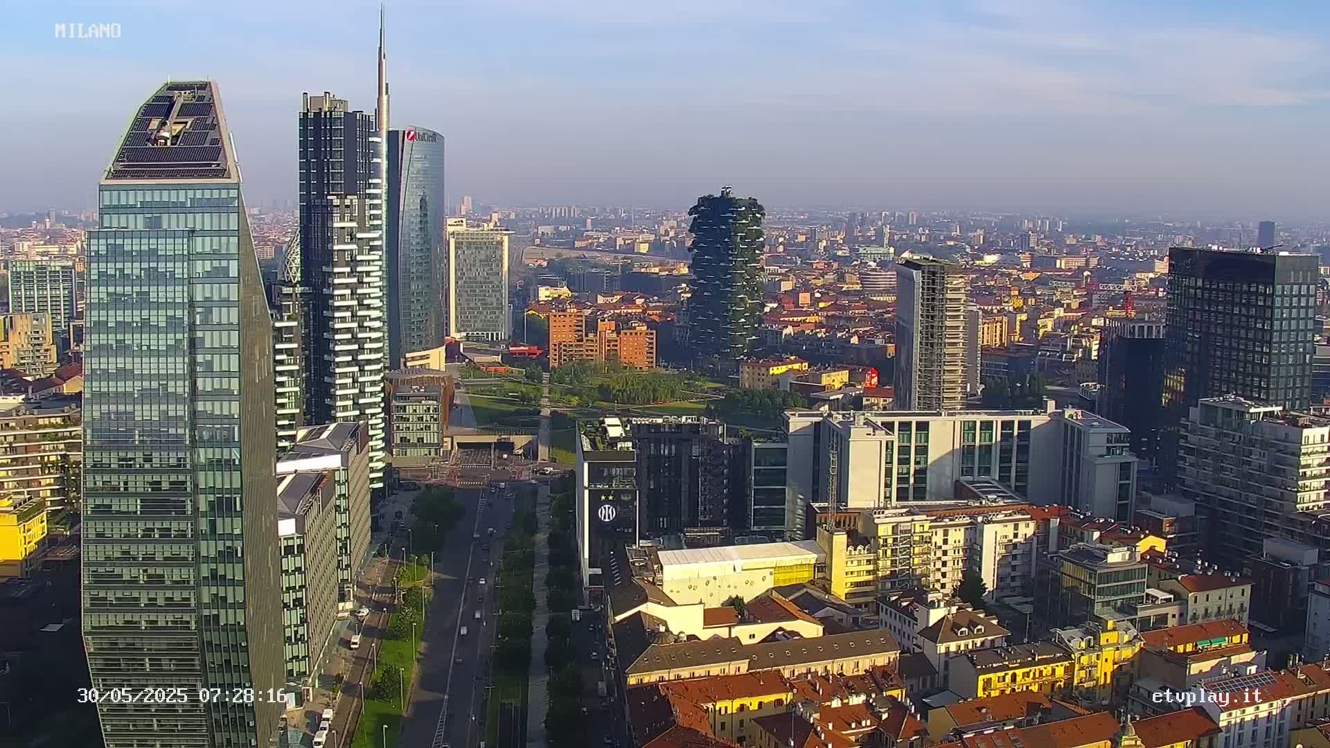 An aerial view of a dense cityscape with numerous skyscrapers, under a clear, bright morning sky.
