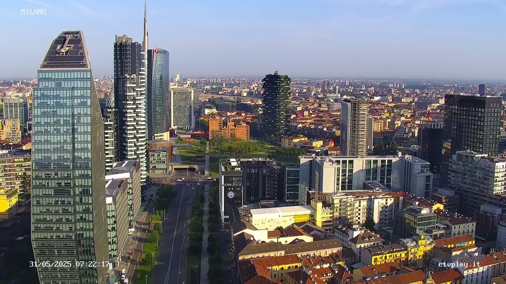 A high-angle, long shot of a city with numerous skyscrapers under a clear, sunny sky.