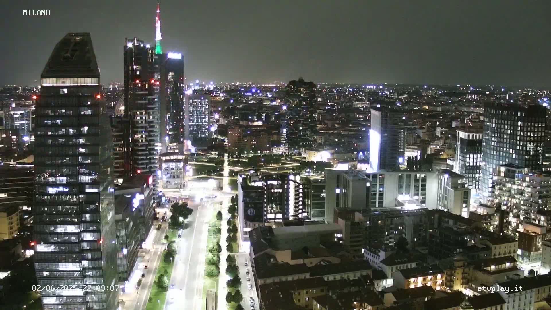 A nighttime aerial view of a city, showing numerous illuminated buildings and streets, under a clear sky.