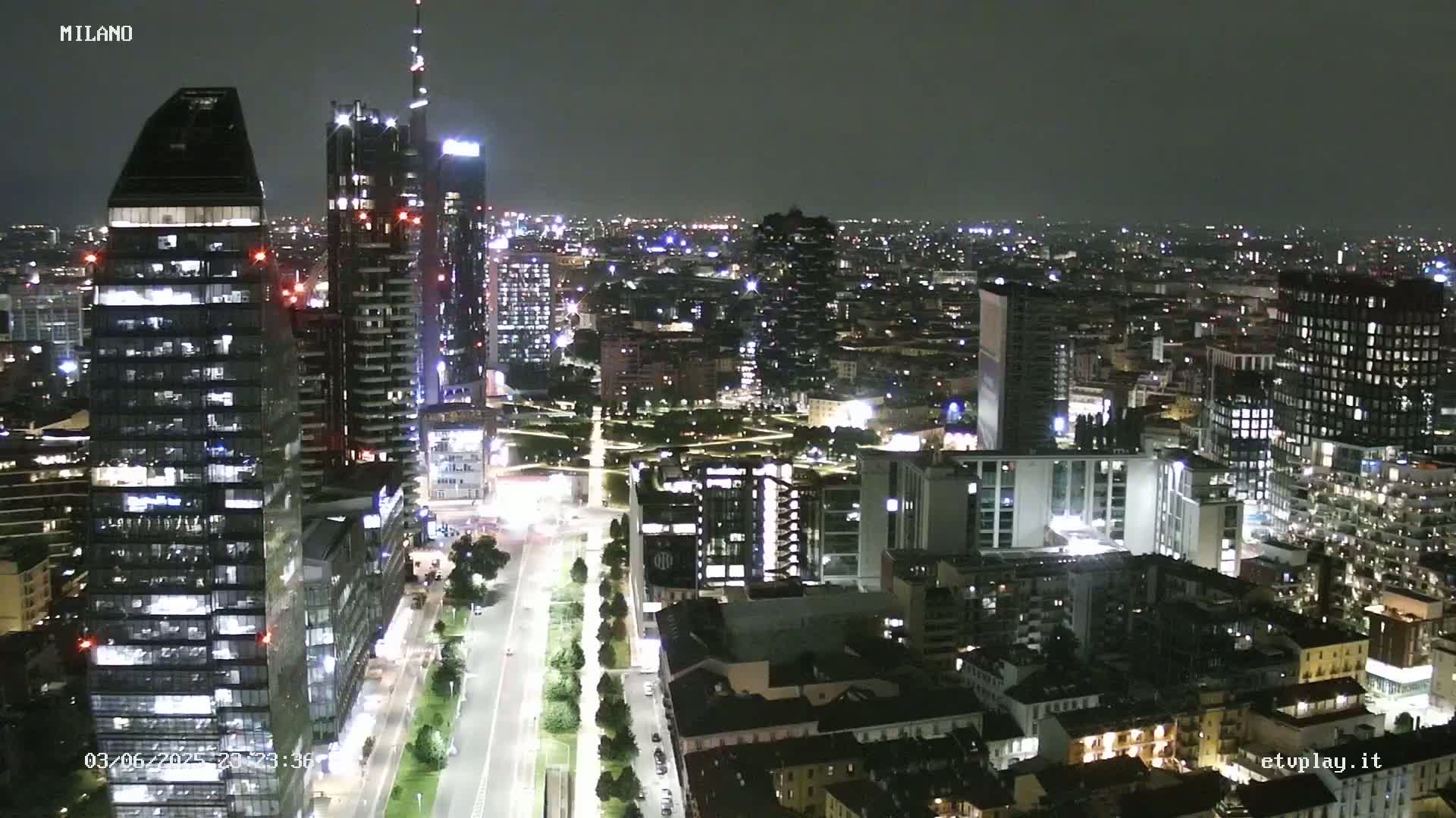 A nighttime aerial view of a city with numerous illuminated buildings and streets, under a clear sky.