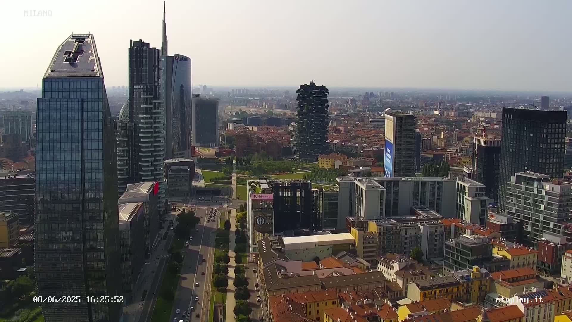 A high-angle, long shot of a city skyline on a hazy day, showing numerous modern and traditional buildings, with a long road visible between them.