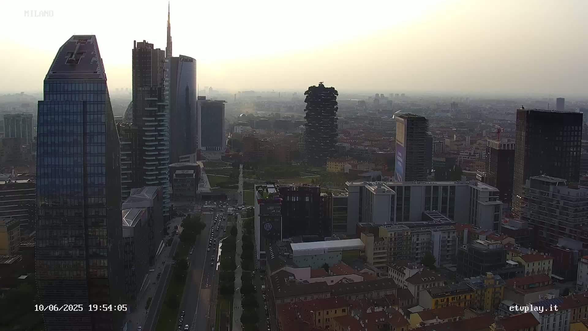 A hazy cityscape of numerous skyscrapers and buildings, viewed from above on a partly cloudy day.