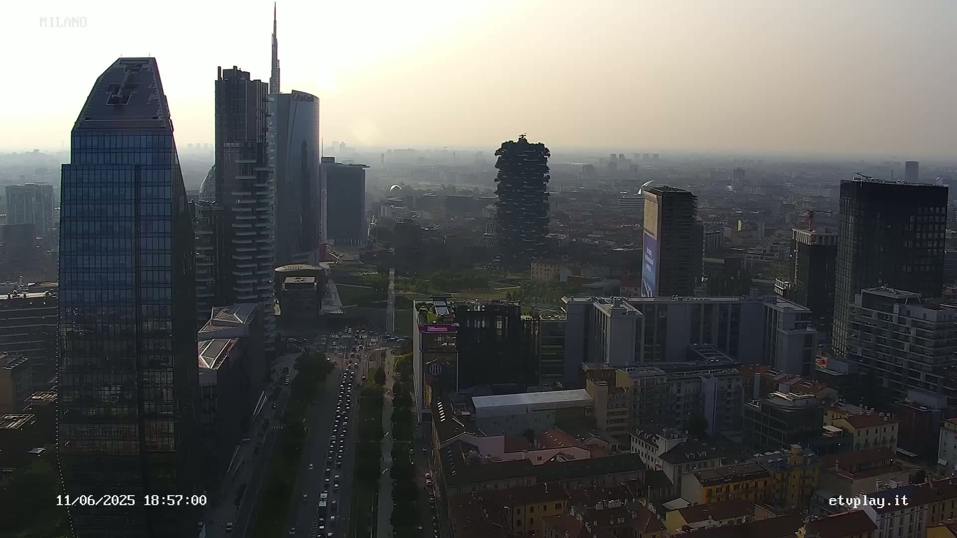 An aerial view of a city skyline on a hazy day, showing numerous skyscrapers and a street with traffic below.