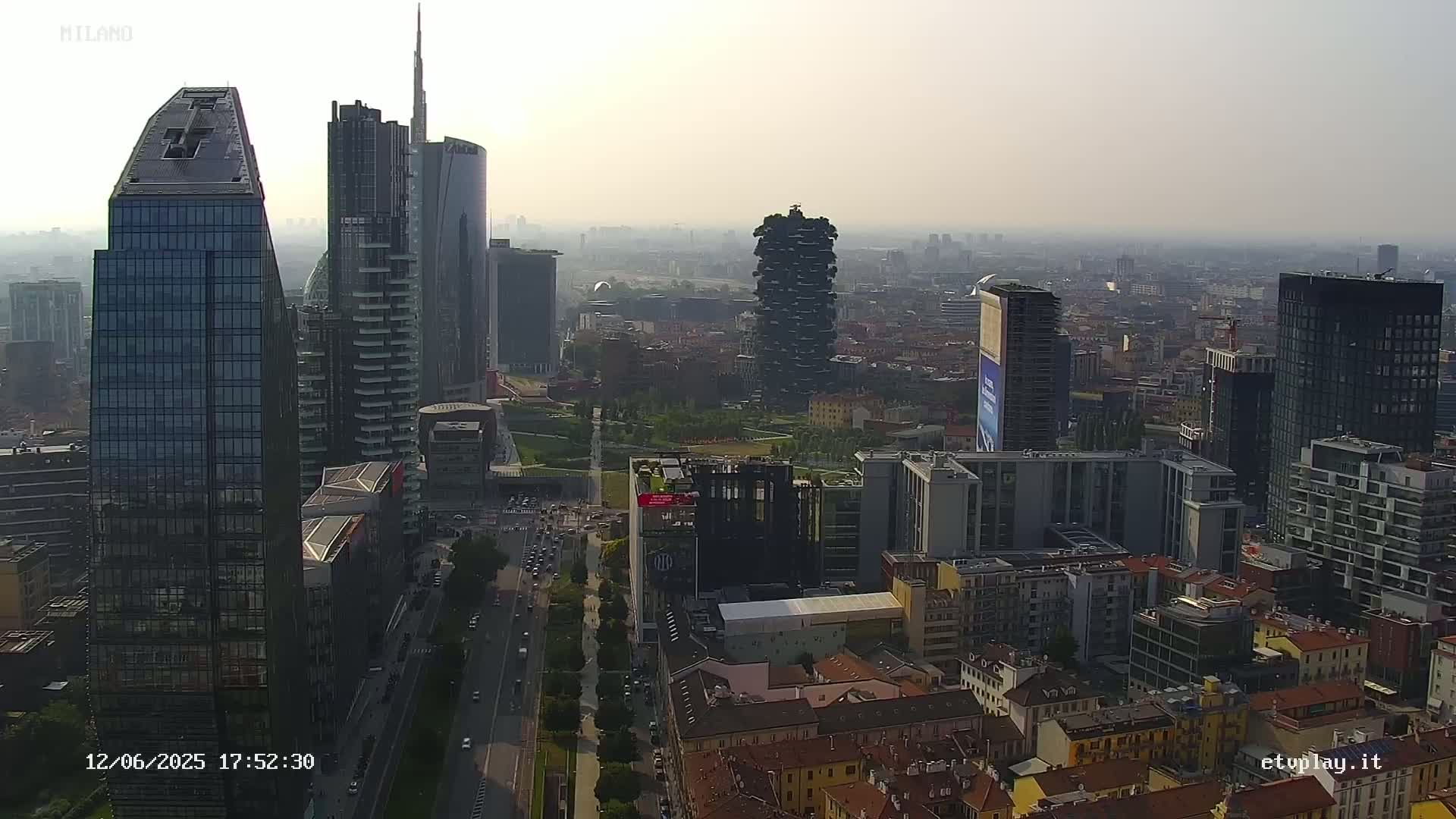 A hazy, high-angle view shows numerous modern and traditional buildings in a dense urban area, with a highway visible in the foreground.