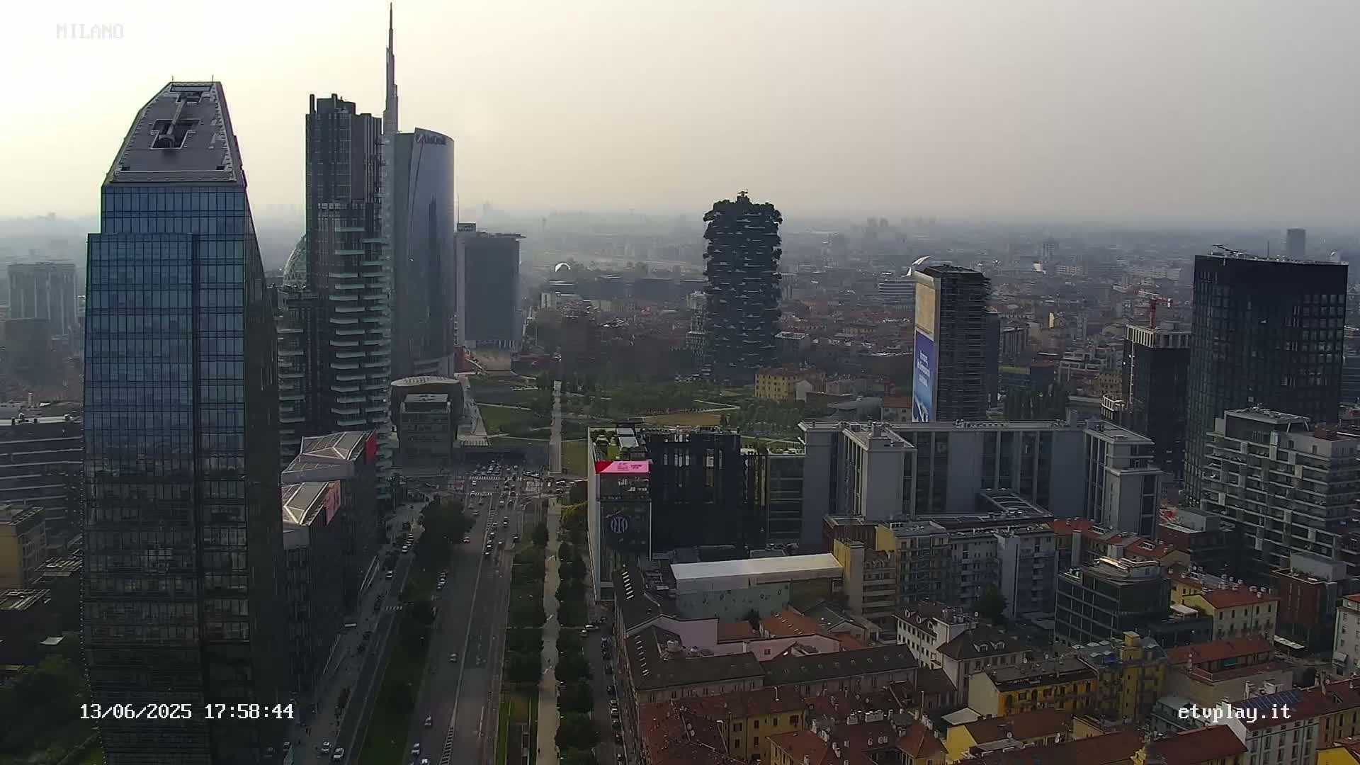 A hazy view of a city skyline, showing numerous skyscrapers and a street below, on a mostly clear day.