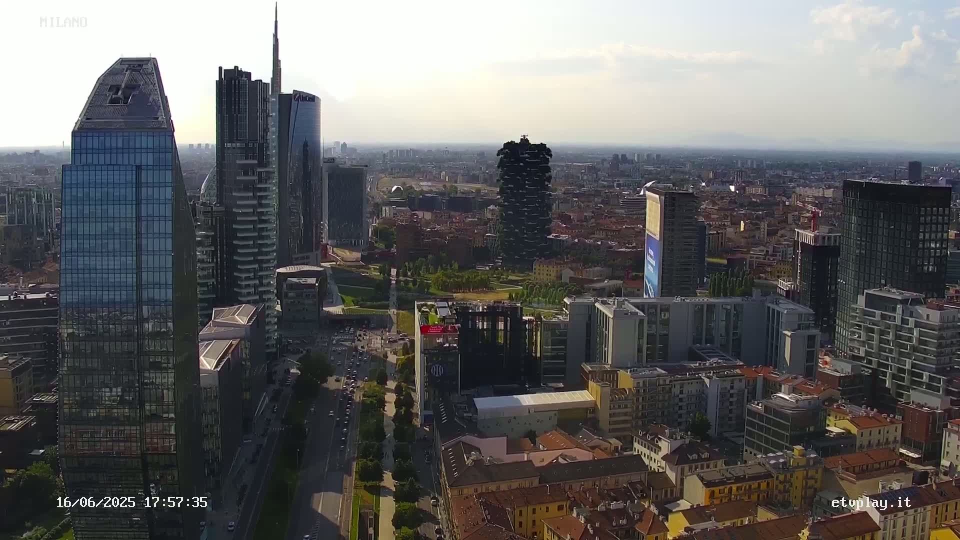 A high-angle, long shot of a city skyline on a partly cloudy day, featuring numerous skyscrapers and surrounding low-rise buildings.