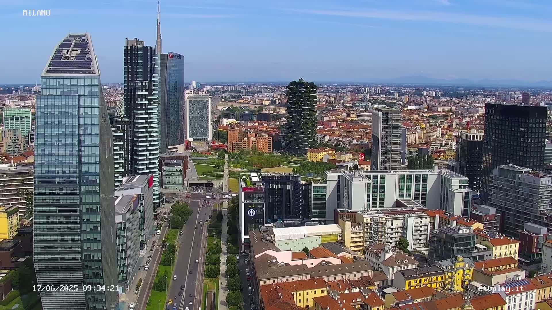 An aerial view of a city's skyline on a sunny day, showing a mix of modern skyscrapers and traditional low-rise buildings.