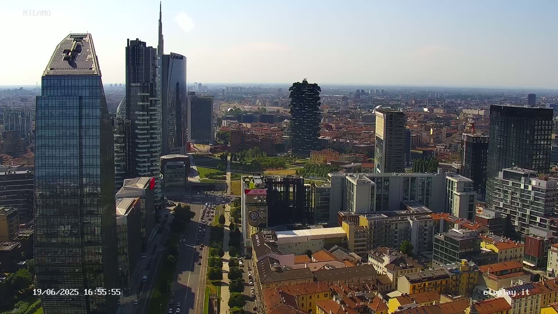 An aerial view of a city skyline on a clear, sunny day, showing numerous skyscrapers and surrounding buildings.