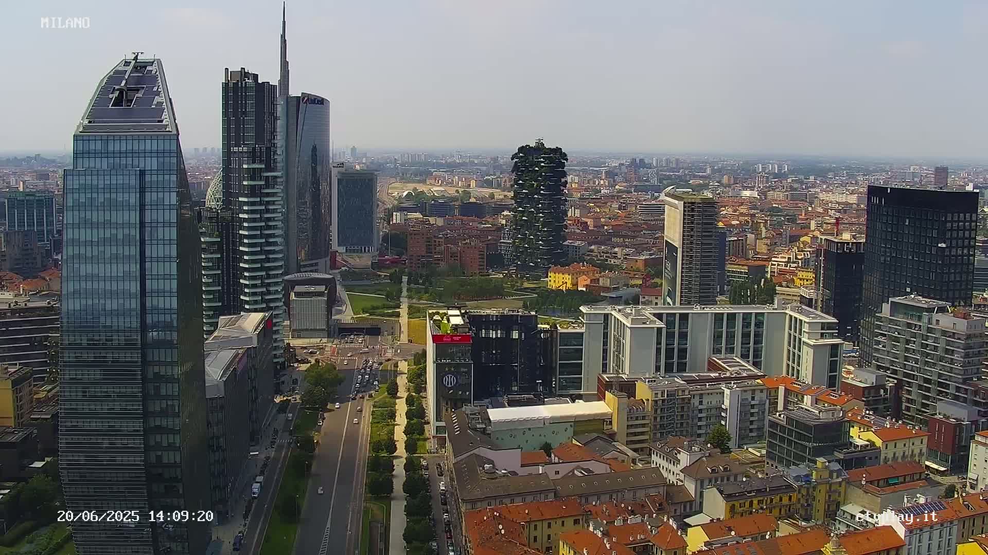 An aerial view shows a city skyline of numerous skyscrapers and high-rise buildings under a hazy sky.