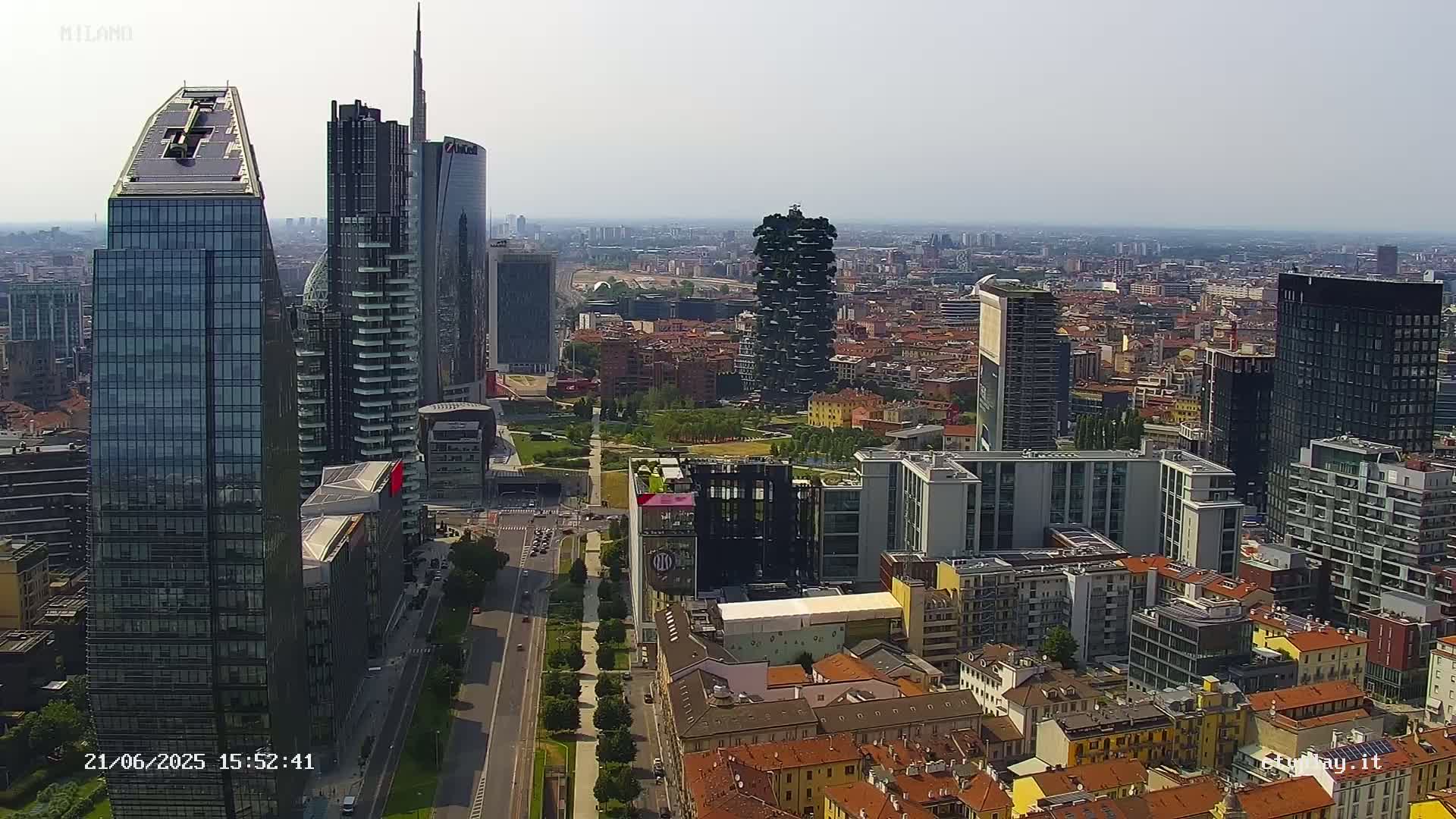 An aerial view of a city skyline on a sunny day, showing numerous skyscrapers and surrounding lower buildings.