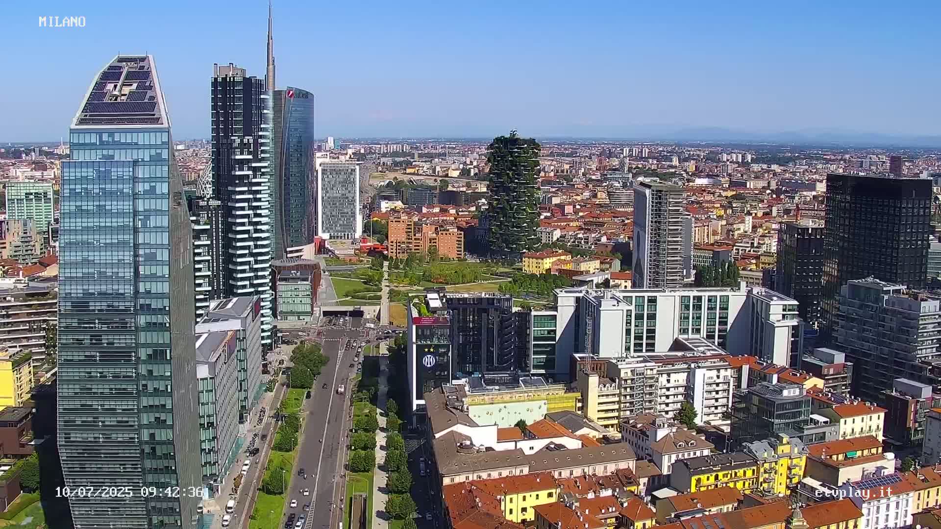 An aerial view of a city with numerous skyscrapers under a clear blue sky, showing a mix of modern high-rises and older, lower buildings.