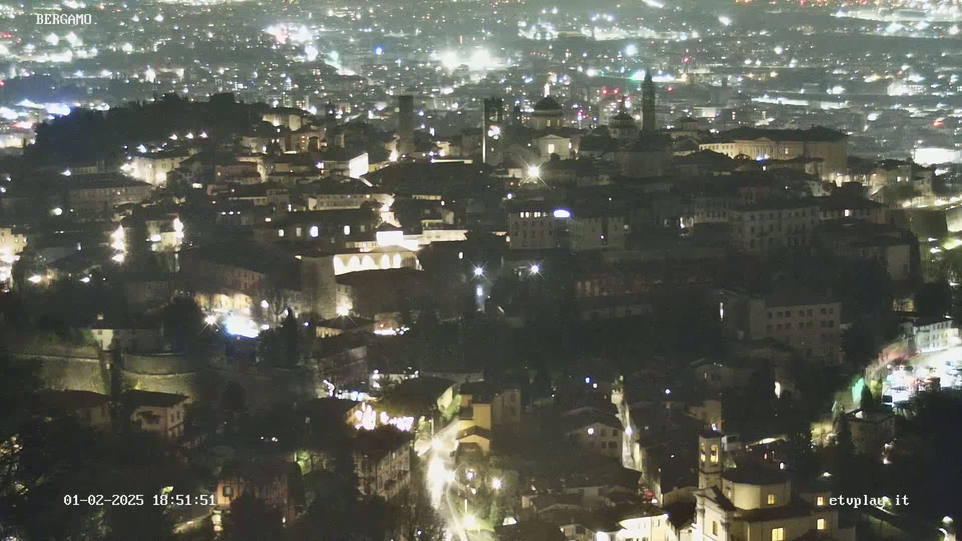 A nighttime aerial view of a city, showing illuminated buildings and streets.