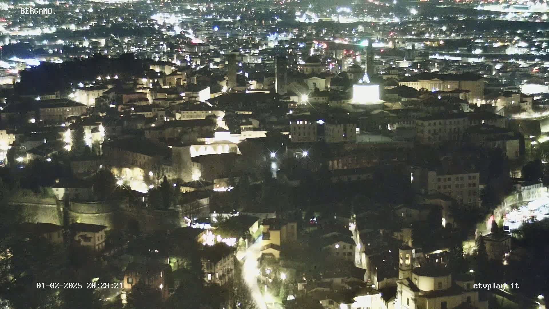 A nighttime aerial view of a city illuminated by streetlights, showing a dense collection of buildings nestled together.