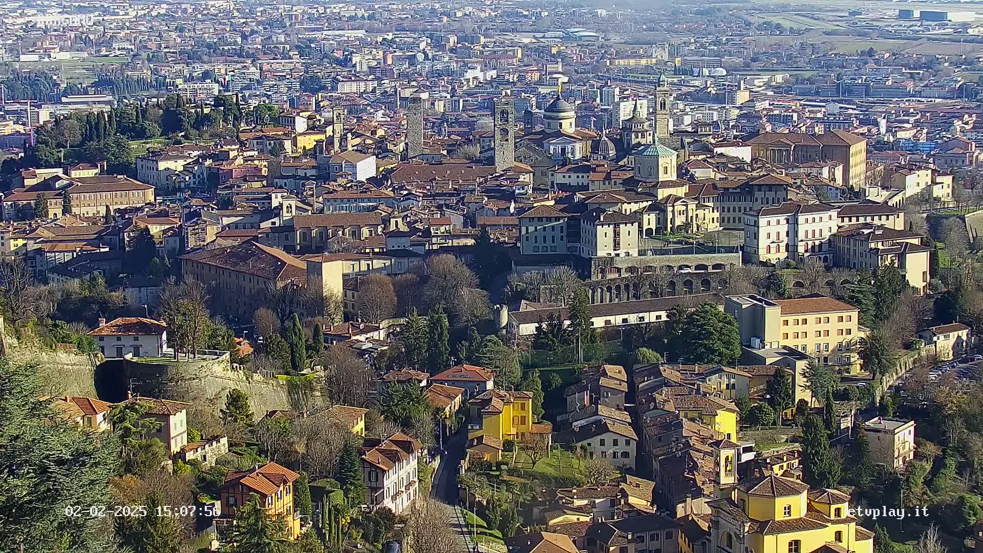 A sprawling city of closely packed buildings with red-tiled roofs, nestled in a valley on a sunny day.