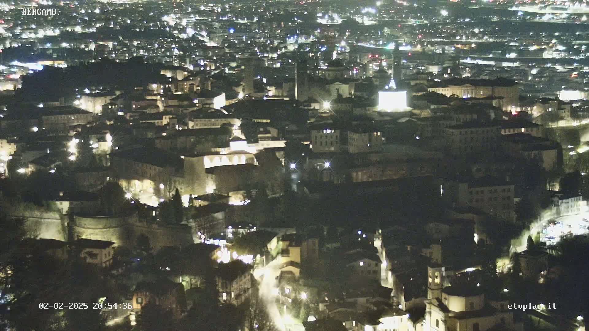 A nighttime aerial view of a city, showing many buildings illuminated by lights.