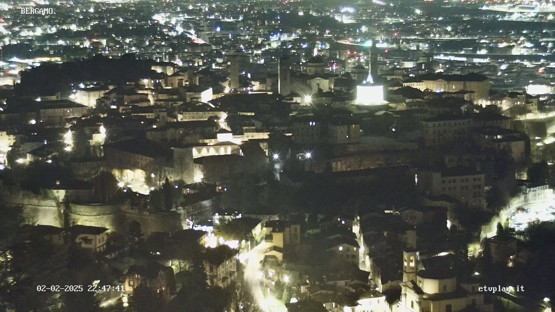 A nighttime aerial view shows a city illuminated by lights, with a dark sky.