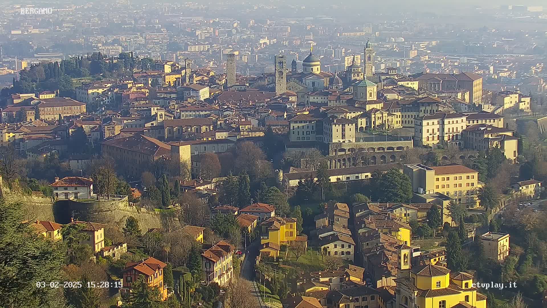A hazy, high-angle view of a sprawling city with numerous buildings, including churches with domes and towers, situated on a hill.