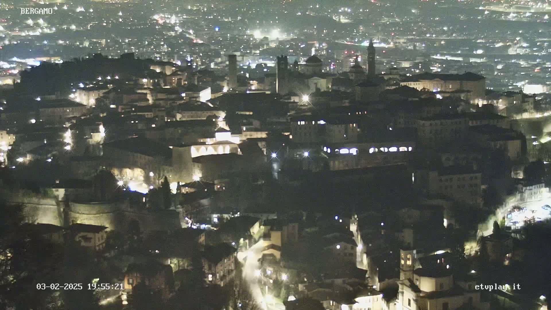 A nighttime, aerial view of a city with many lights illuminating buildings and streets.