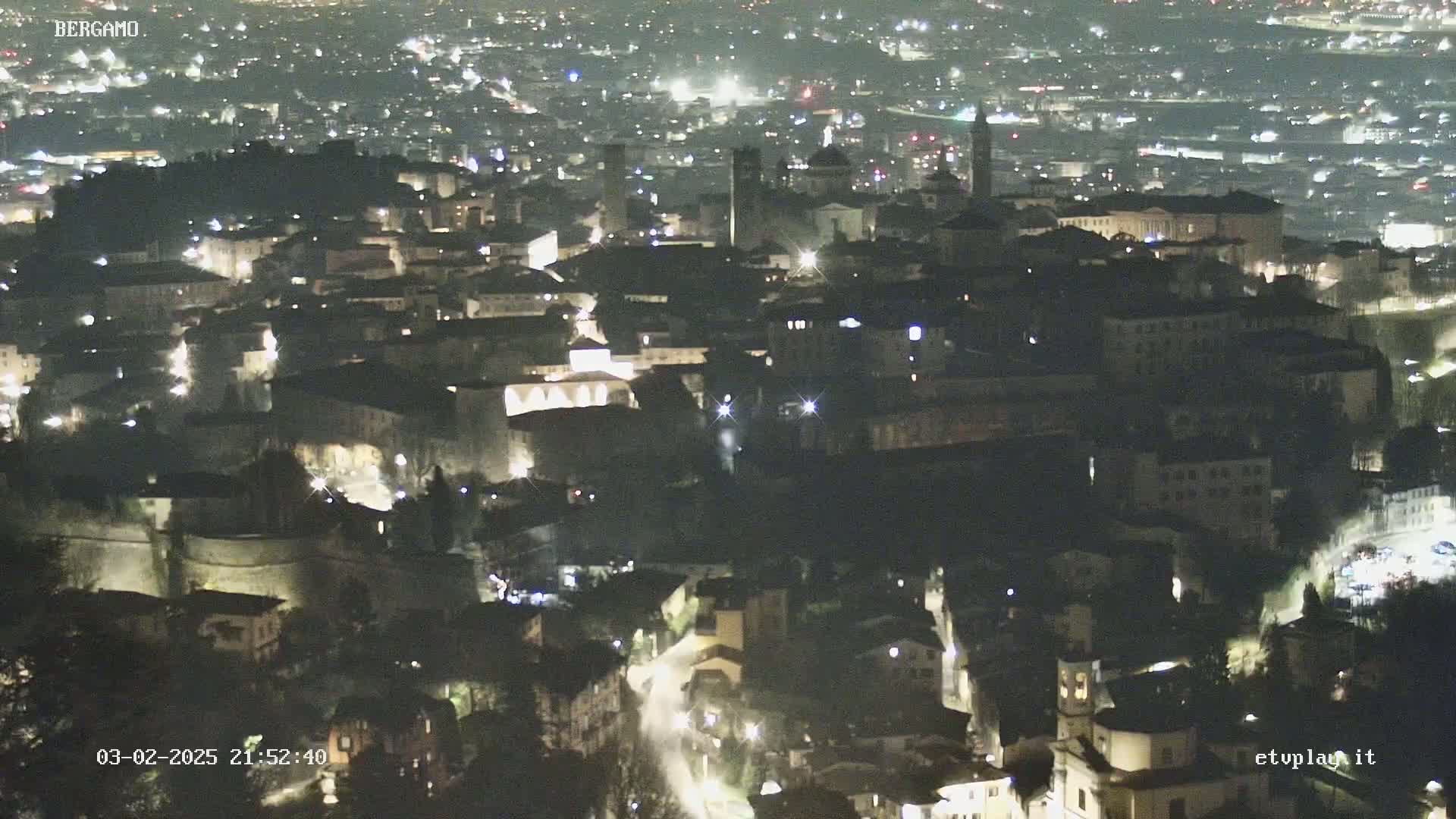 A nighttime, high-angle view of a city with many buildings illuminated by lights.