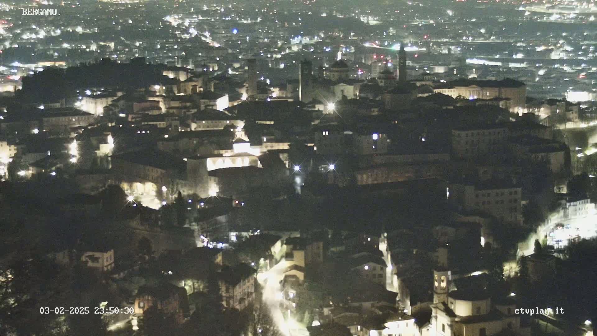 A nighttime, aerial view of a city with many buildings illuminated by streetlights.
