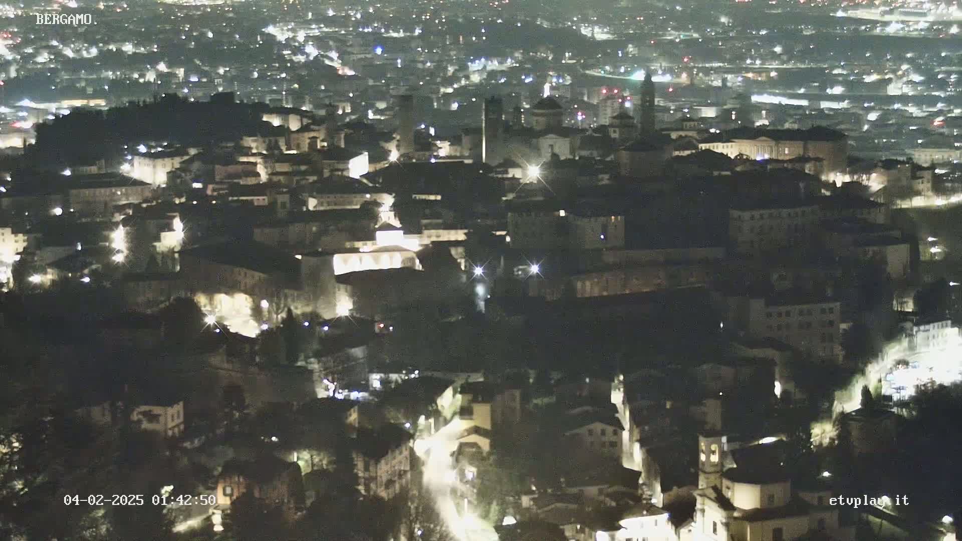 A nighttime, high-angle view of a city with numerous illuminated buildings and streets.