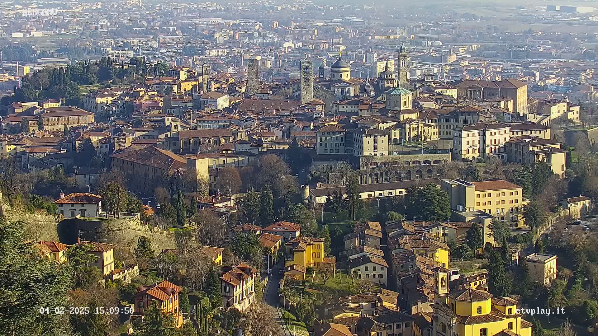 A sprawling city with numerous buildings of varying heights and architectural styles, nestled within hillsides under a sunny sky.