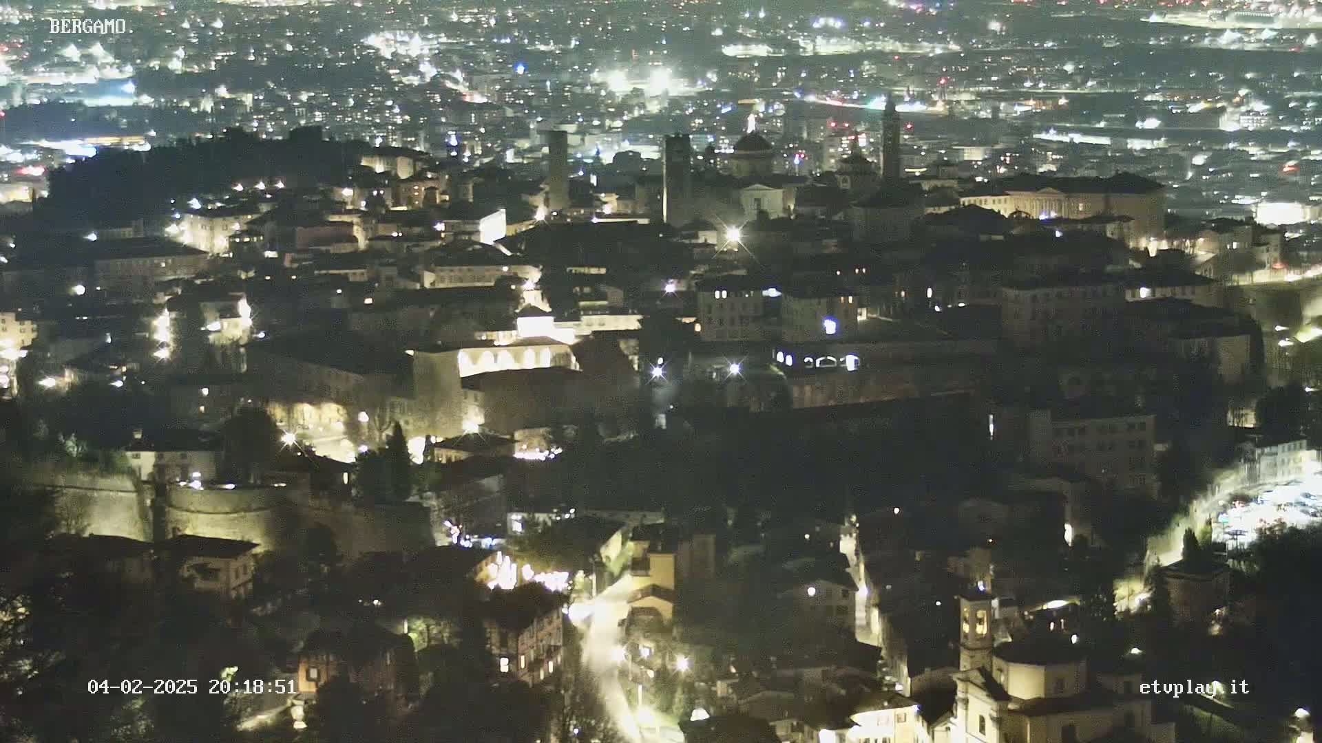 A nighttime, high-angle view of a city illuminated by streetlights, showing a dense collection of buildings nestled against a hill.