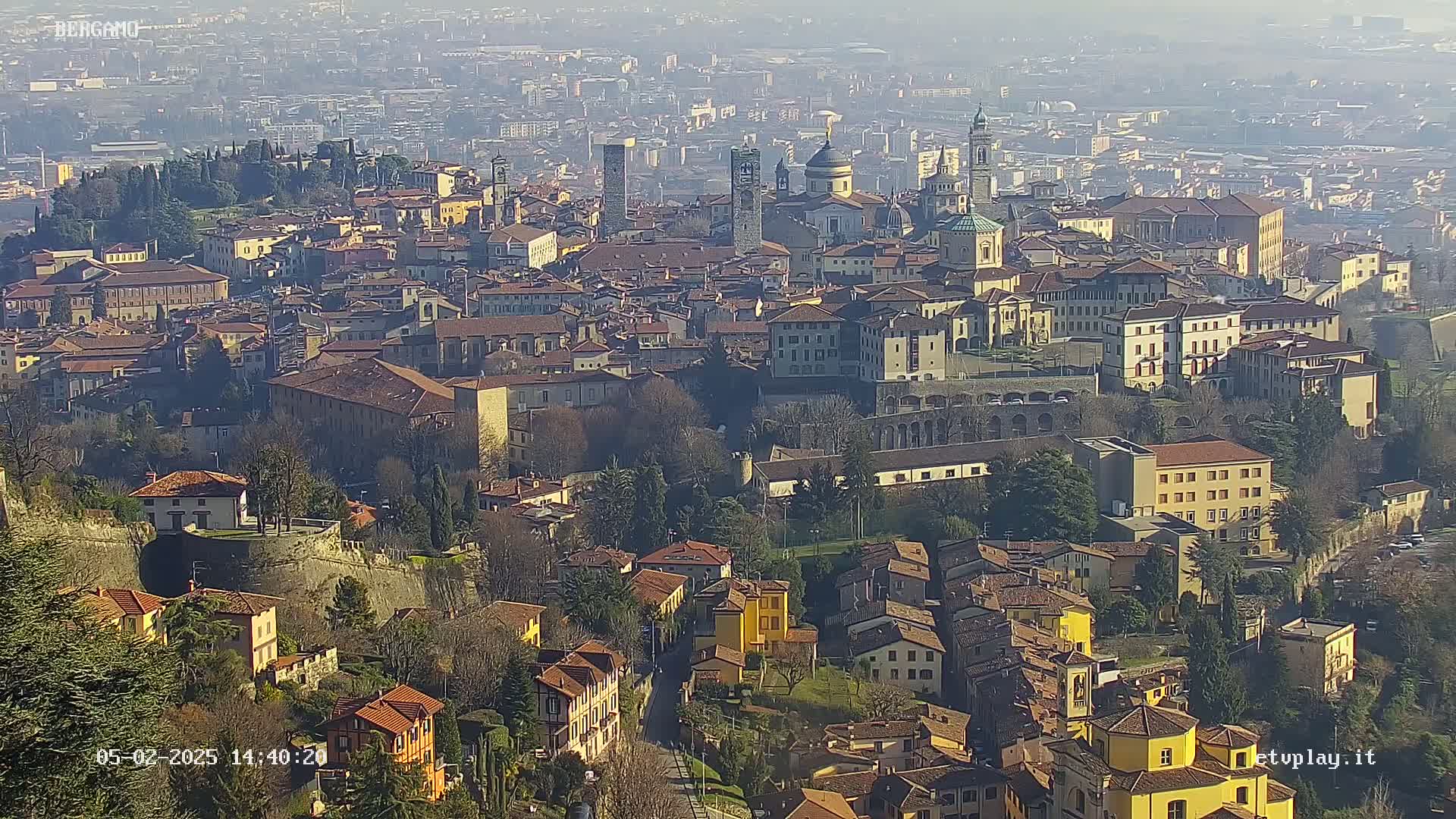 A sprawling city with numerous buildings of varying sizes and architectural styles, viewed from a high vantage point on a clear, sunny day.