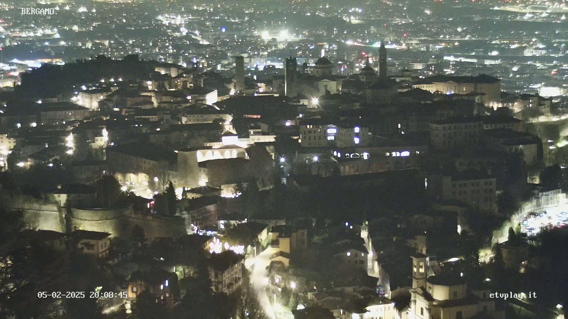 A nighttime aerial view of a city, showing illuminated buildings and streets.