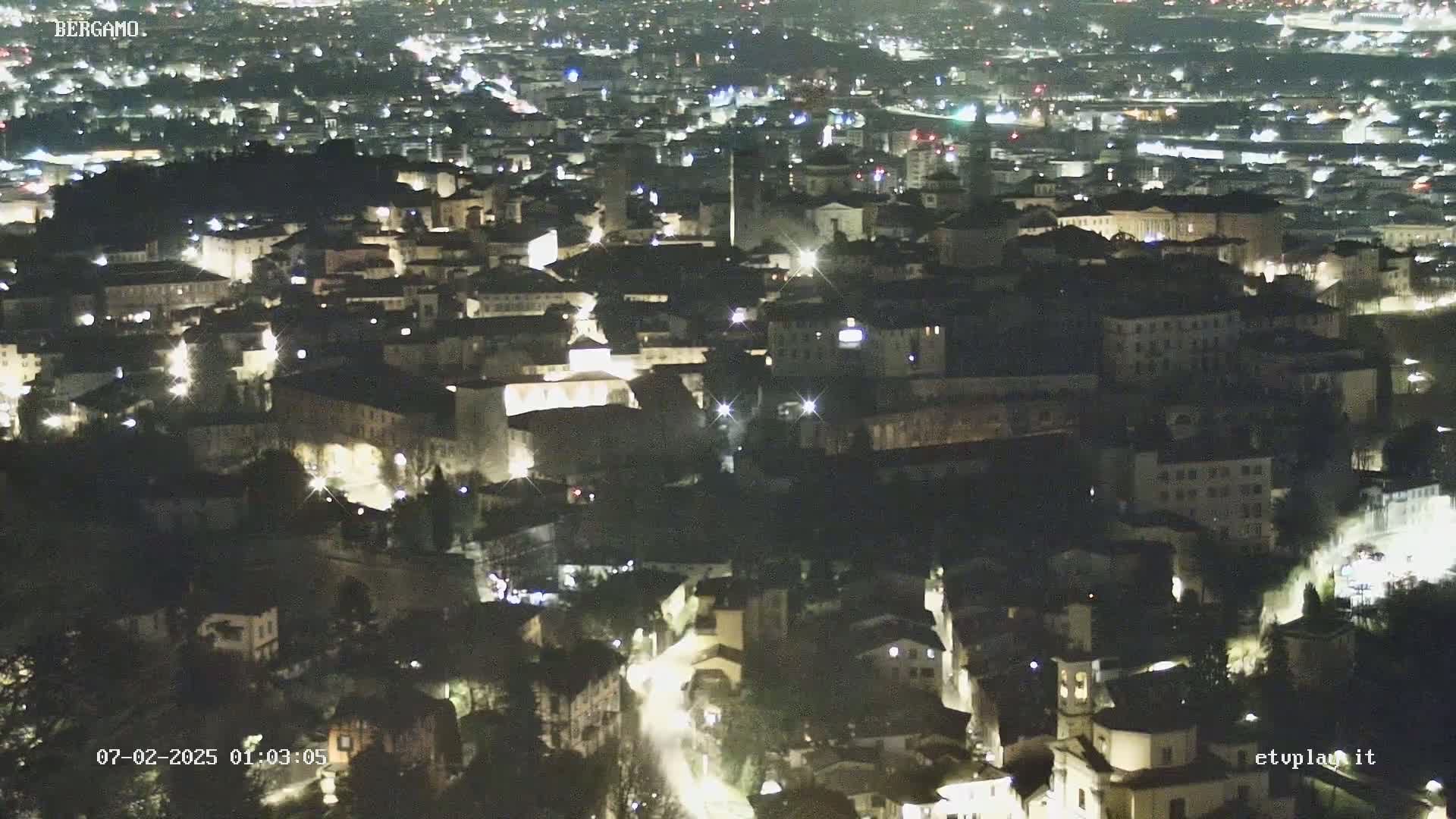 A nighttime aerial view of a city with numerous illuminated buildings and streets.