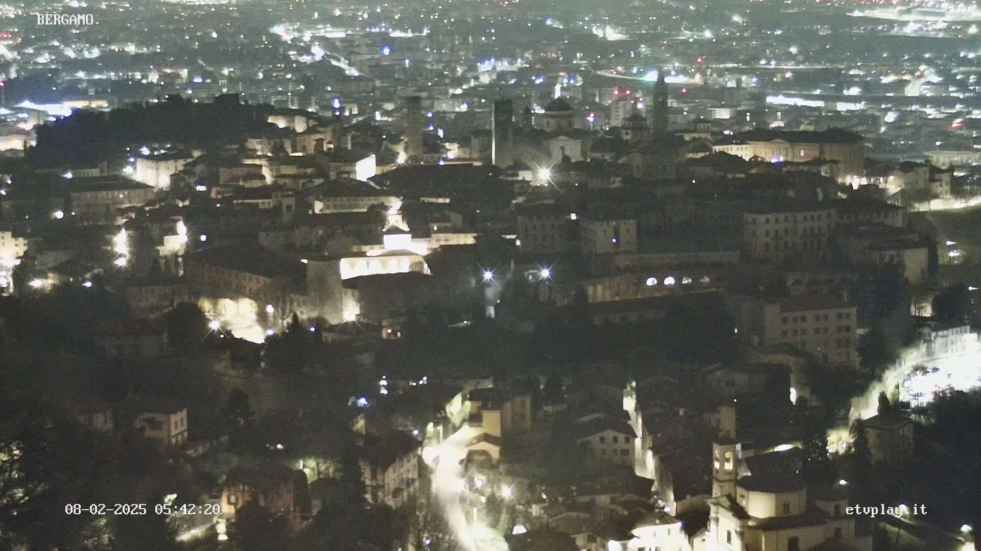 A nighttime, high-angle view of a city, showing numerous illuminated buildings and streets.