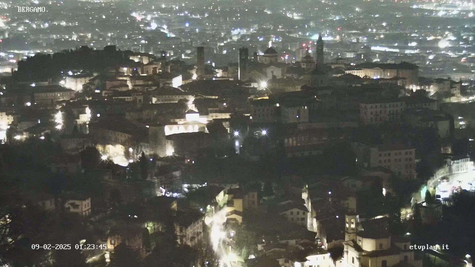 A nighttime, high-angle view of a city with illuminated buildings and streets.