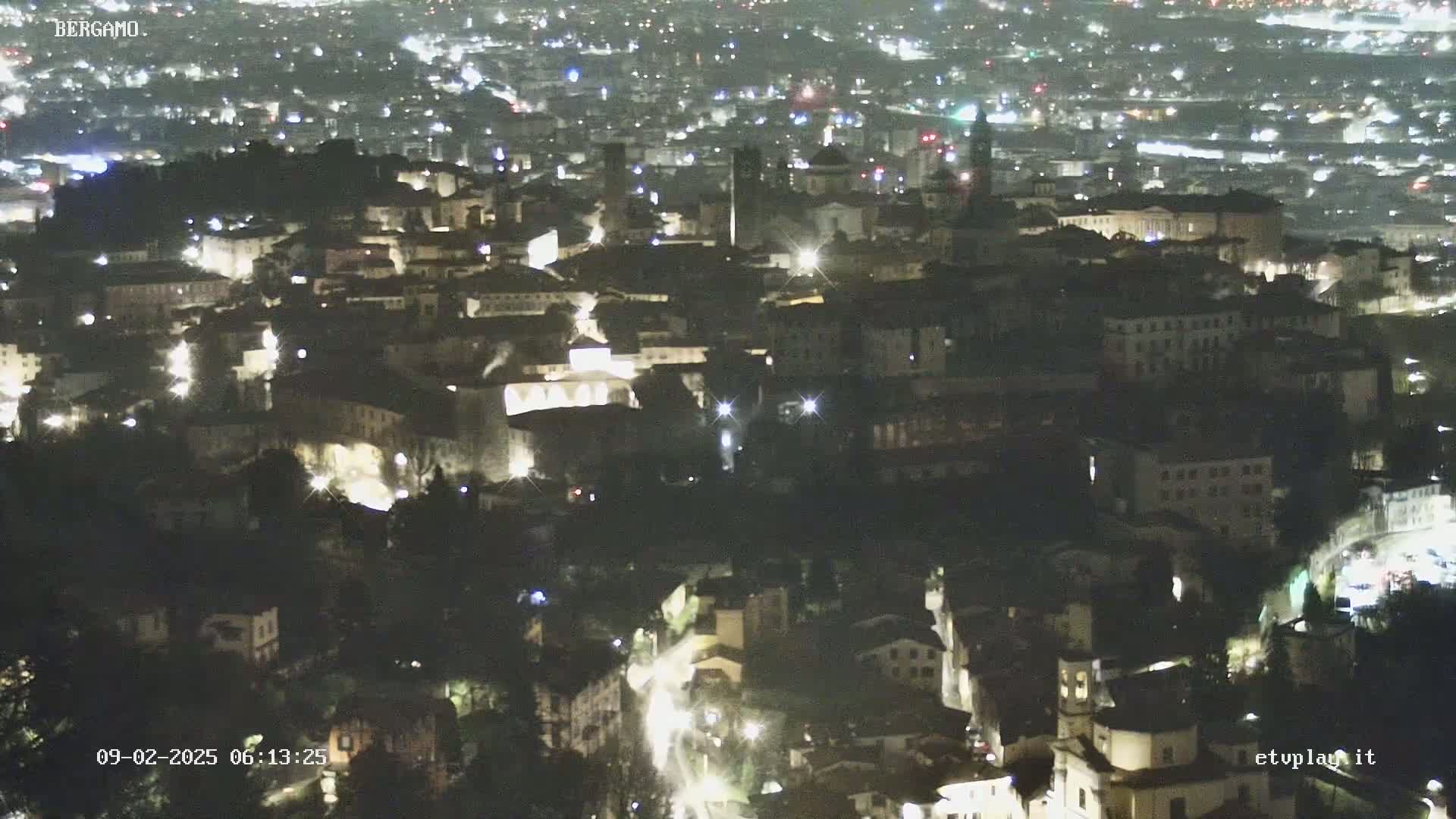 A nighttime aerial view of a city, showing numerous illuminated buildings and streets.