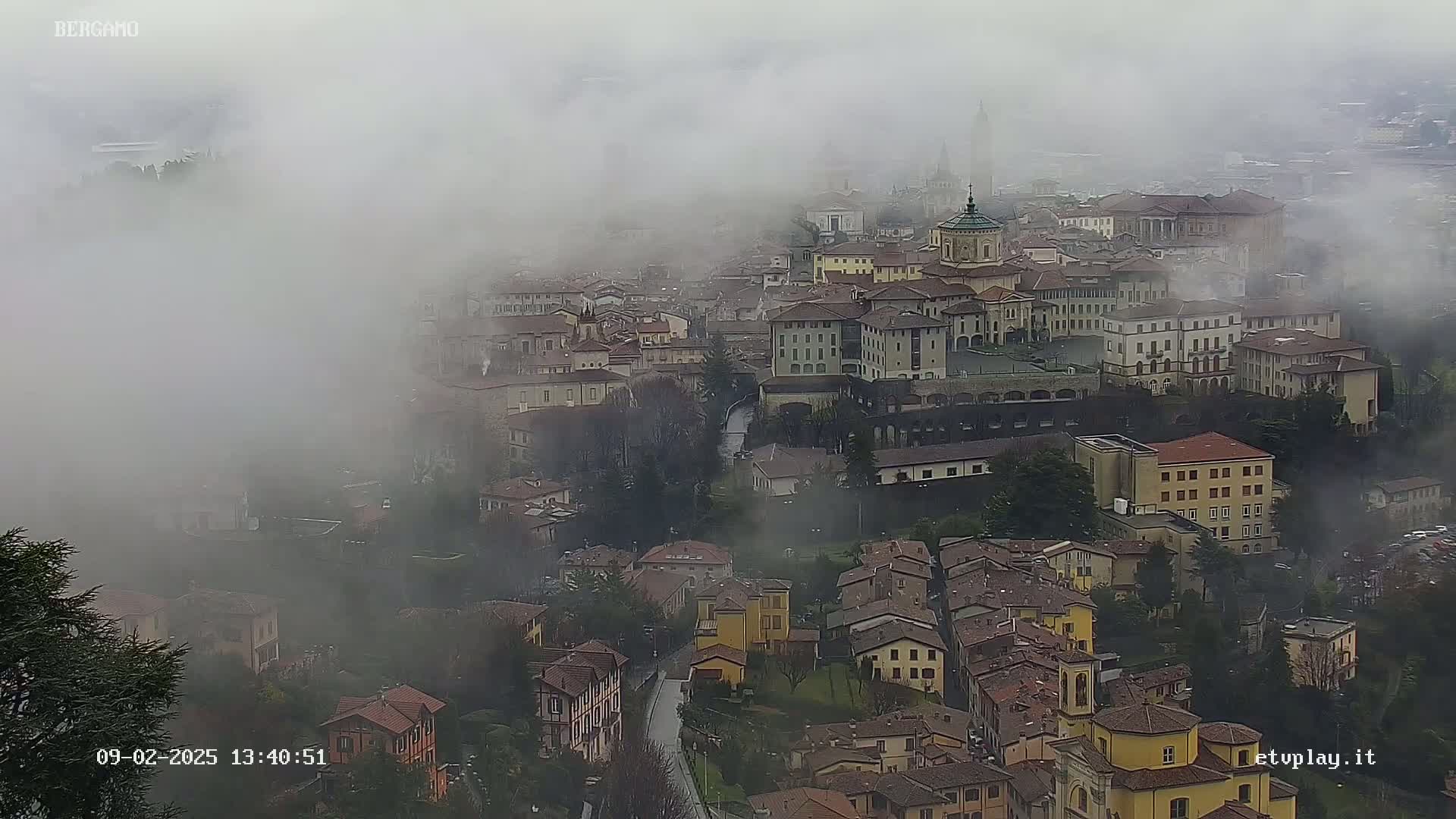 A foggy view of a city with numerous buildings, a river running through it, and surrounding hills.