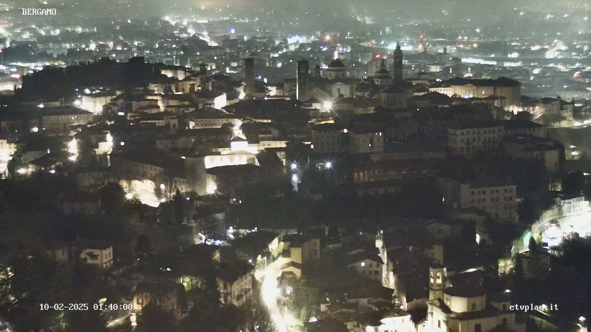 A nighttime, aerial view of a city with many illuminated buildings and streets.