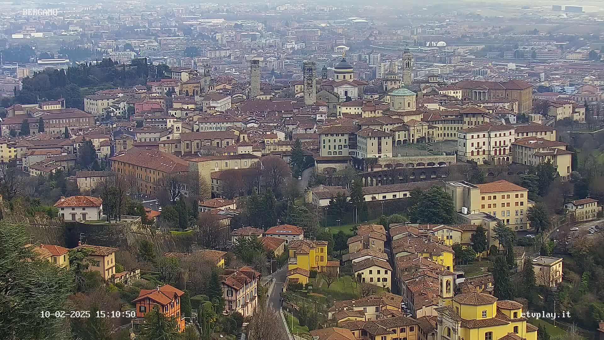 A sprawling city of closely packed, terracotta-roofed buildings sits nestled in a valley on an overcast day.