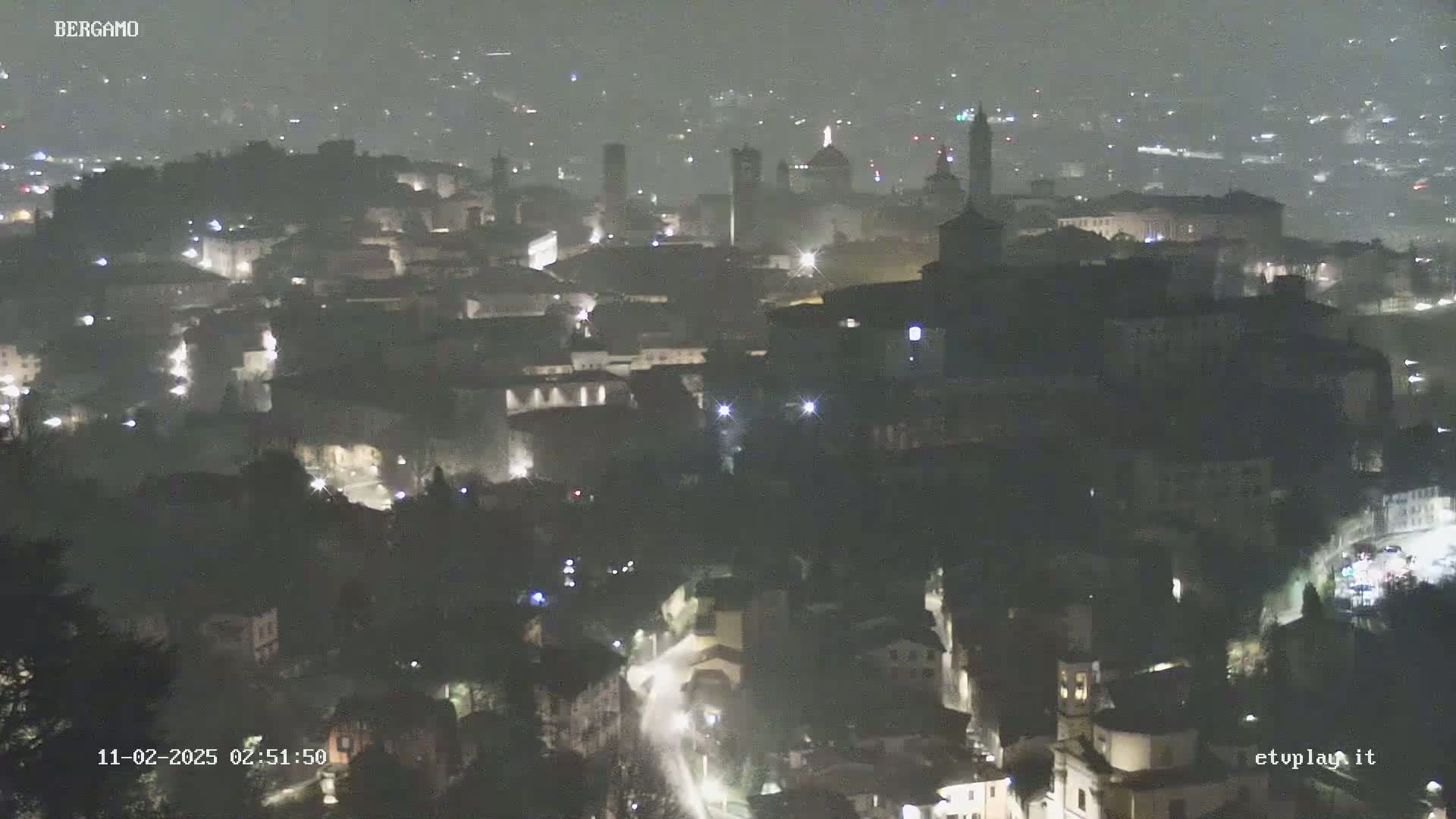 A nighttime, hazy view of a city with numerous lights illuminating buildings and streets.