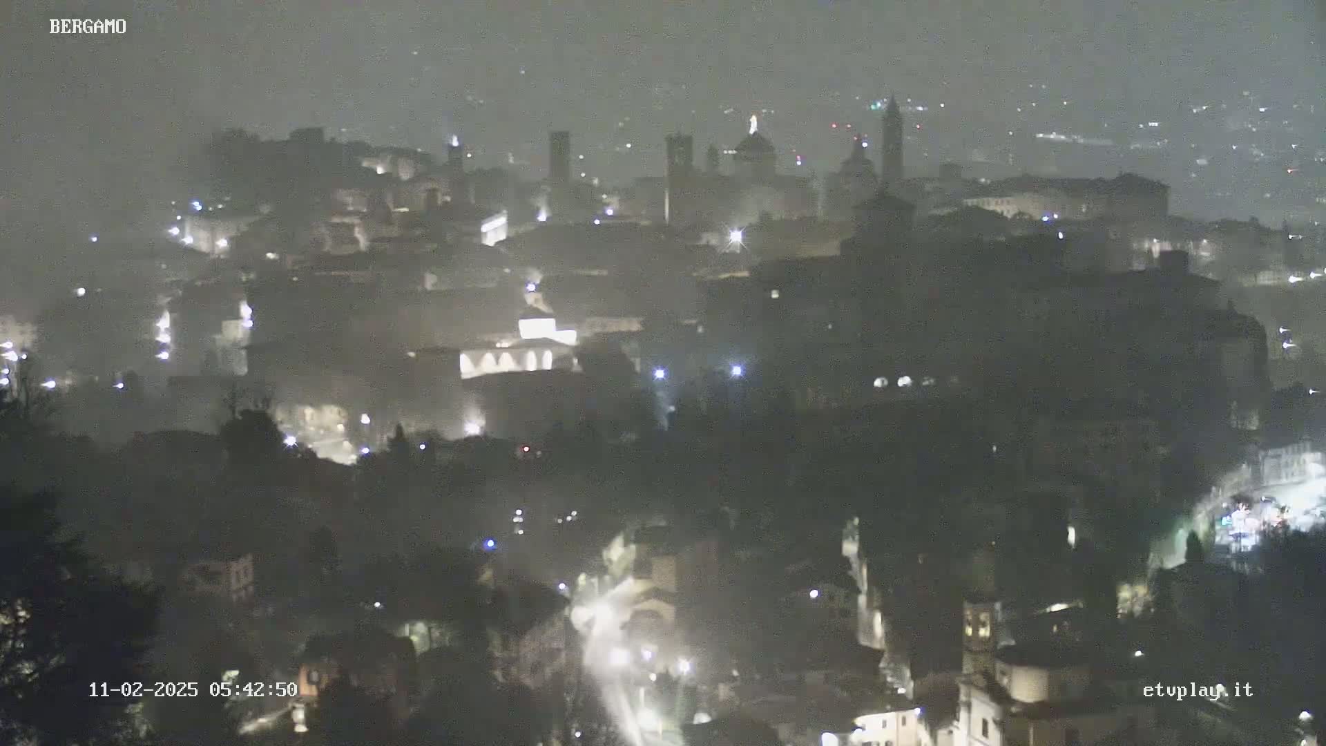 A nighttime, hazy view of a city with dimly lit buildings and streets, seen from a distance.