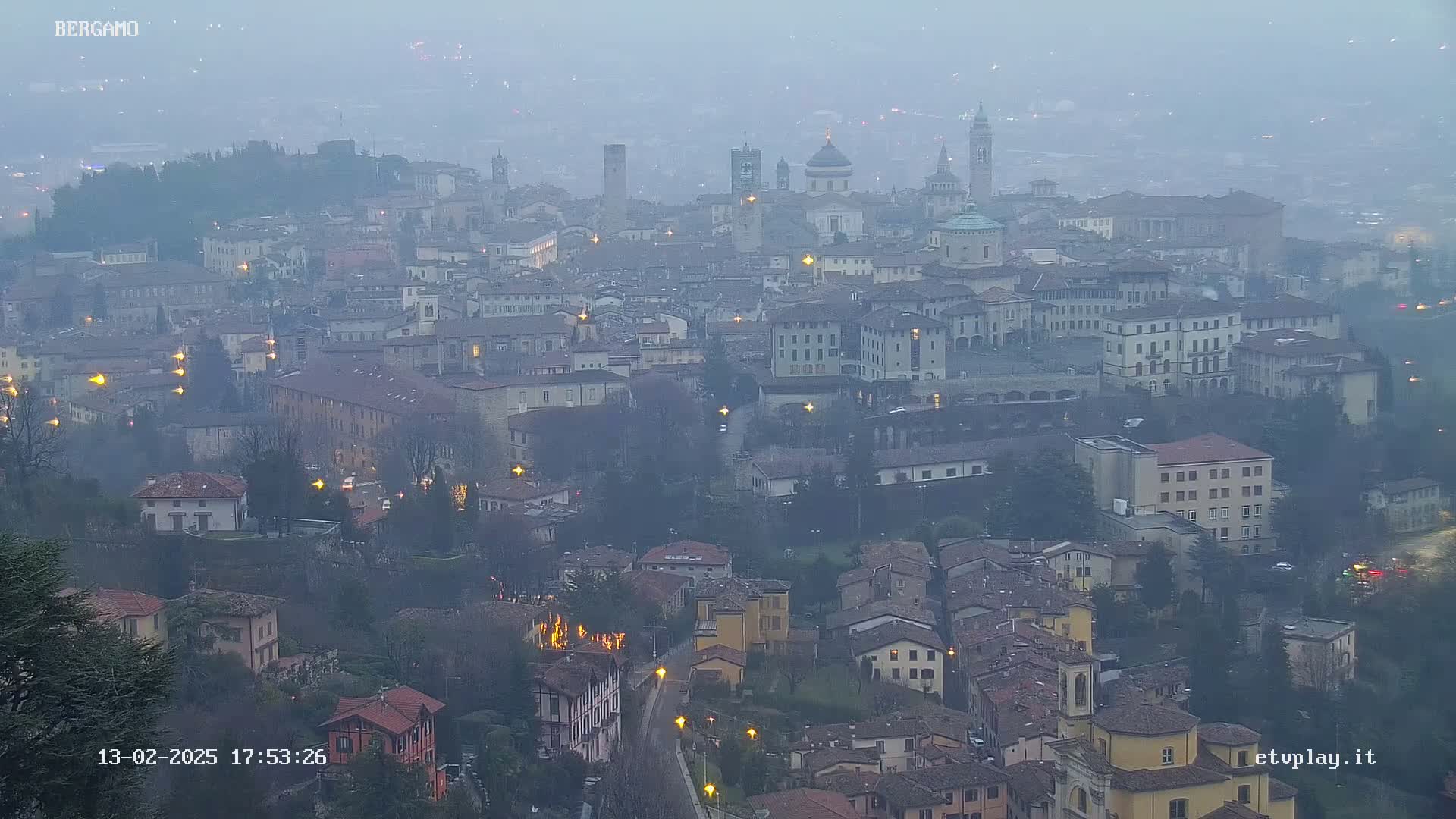 A hazy, twilight view overlooks a sprawling city with numerous buildings and illuminated streetlights.