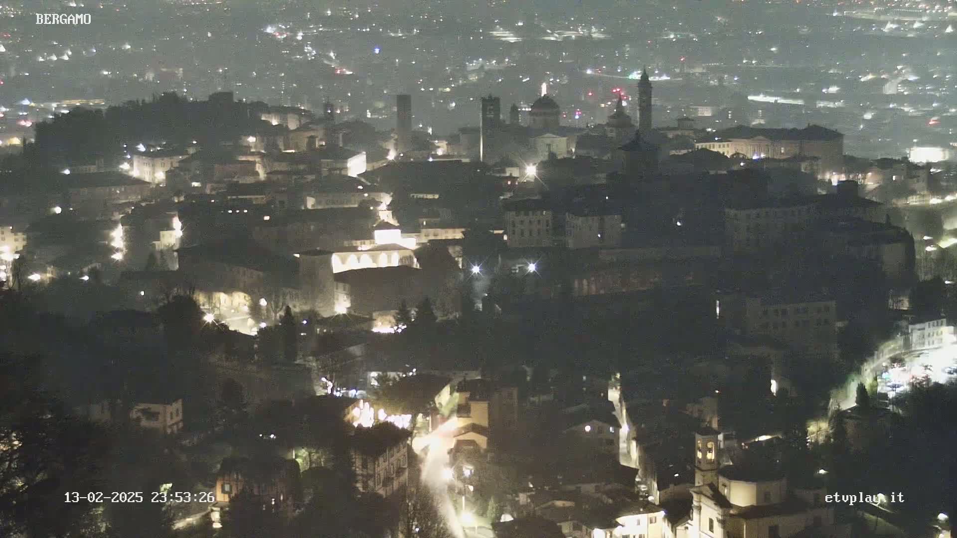 A nighttime aerial view of a city, showing dimly lit buildings and streets under a hazy sky.