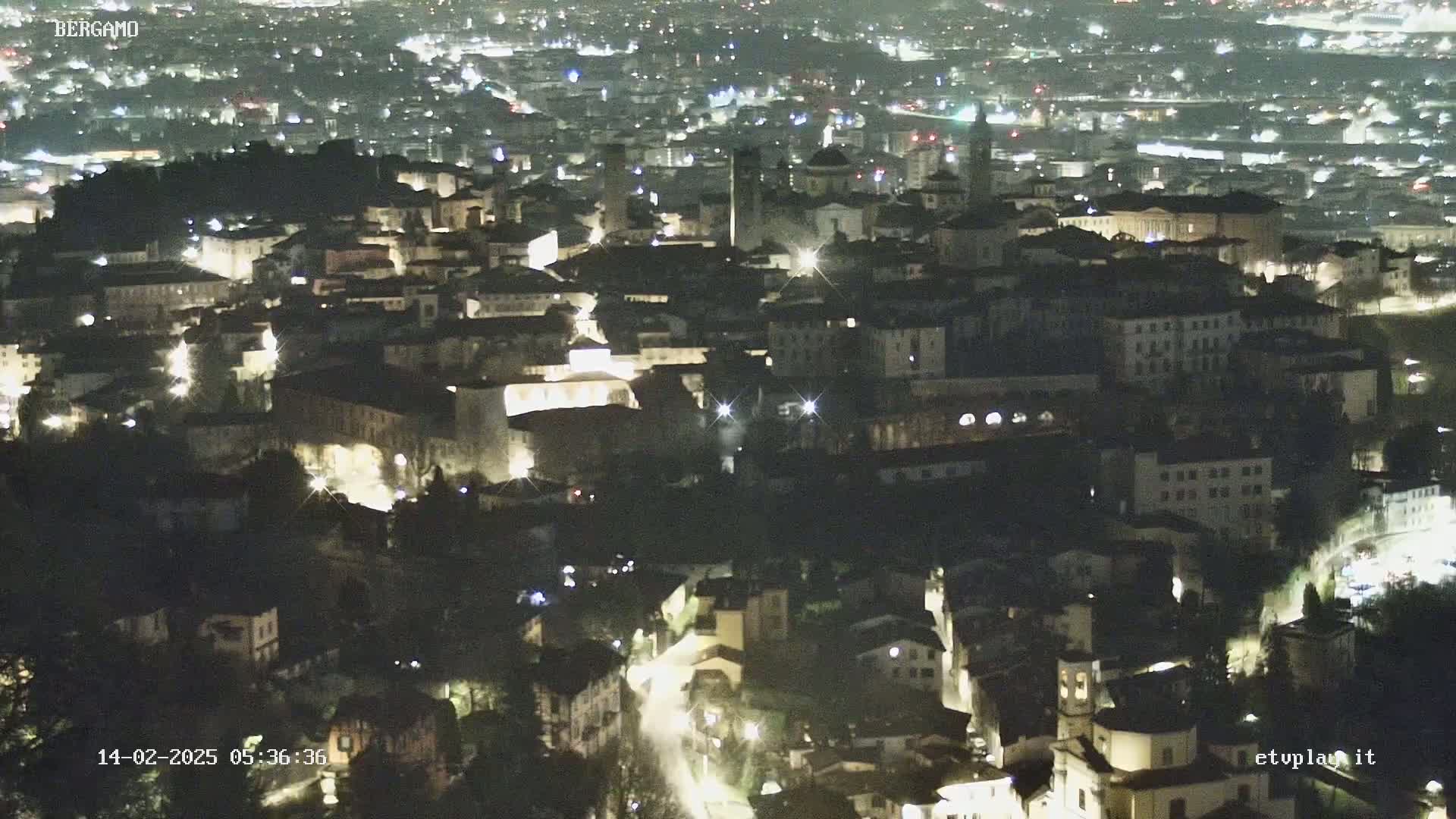 A nighttime, high-angle view of a city with many lights illuminating buildings and streets.