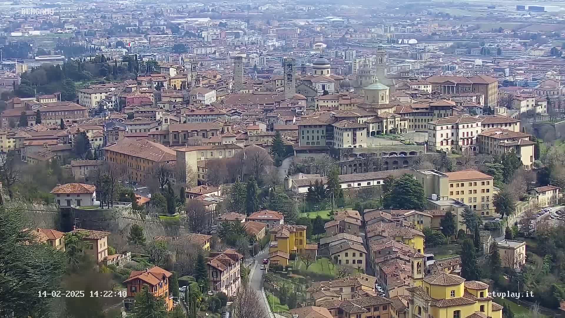 A sprawling city of terracotta-roofed buildings nestled in a valley under a hazy sky.