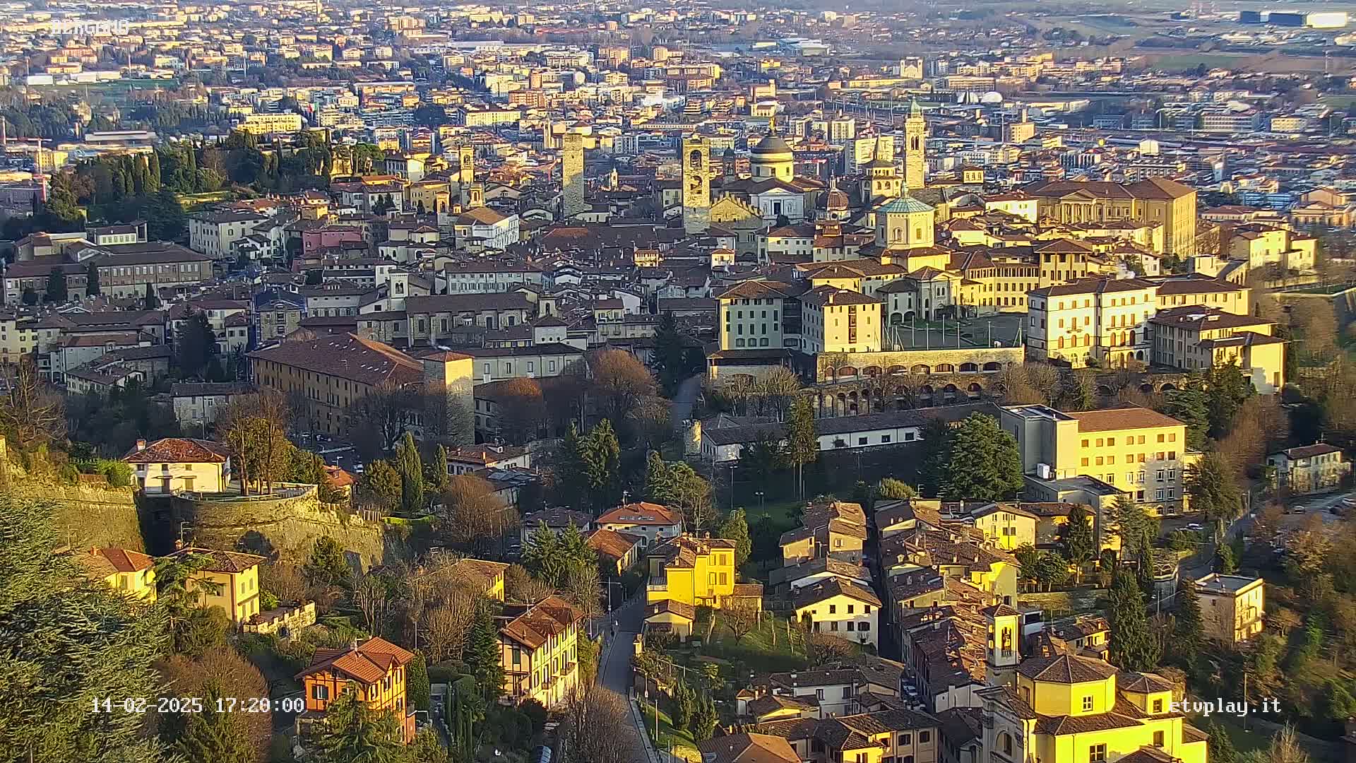 An aerial view of a dense, historic city bathed in the golden light of late afternoon sun.