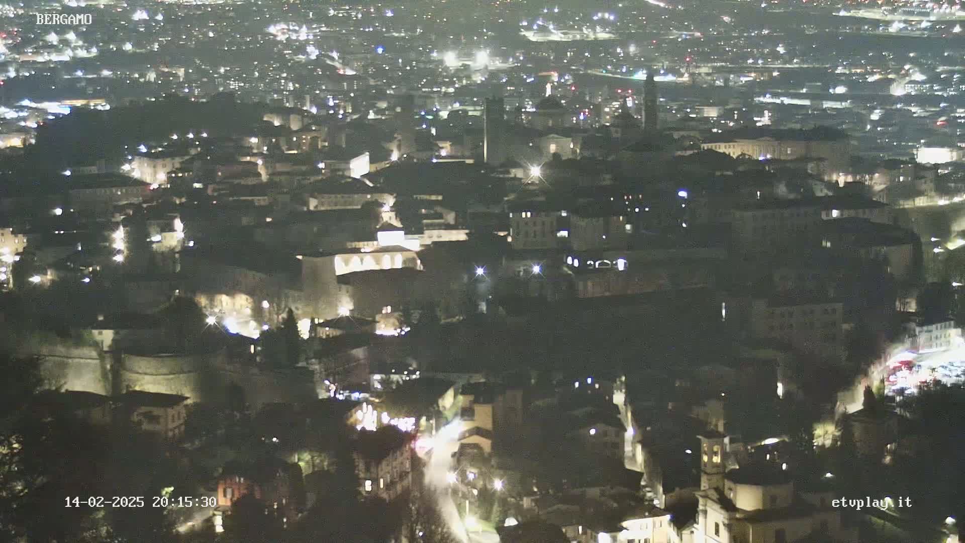 A nighttime, high-angle view of a city with many lights illuminating buildings and streets.