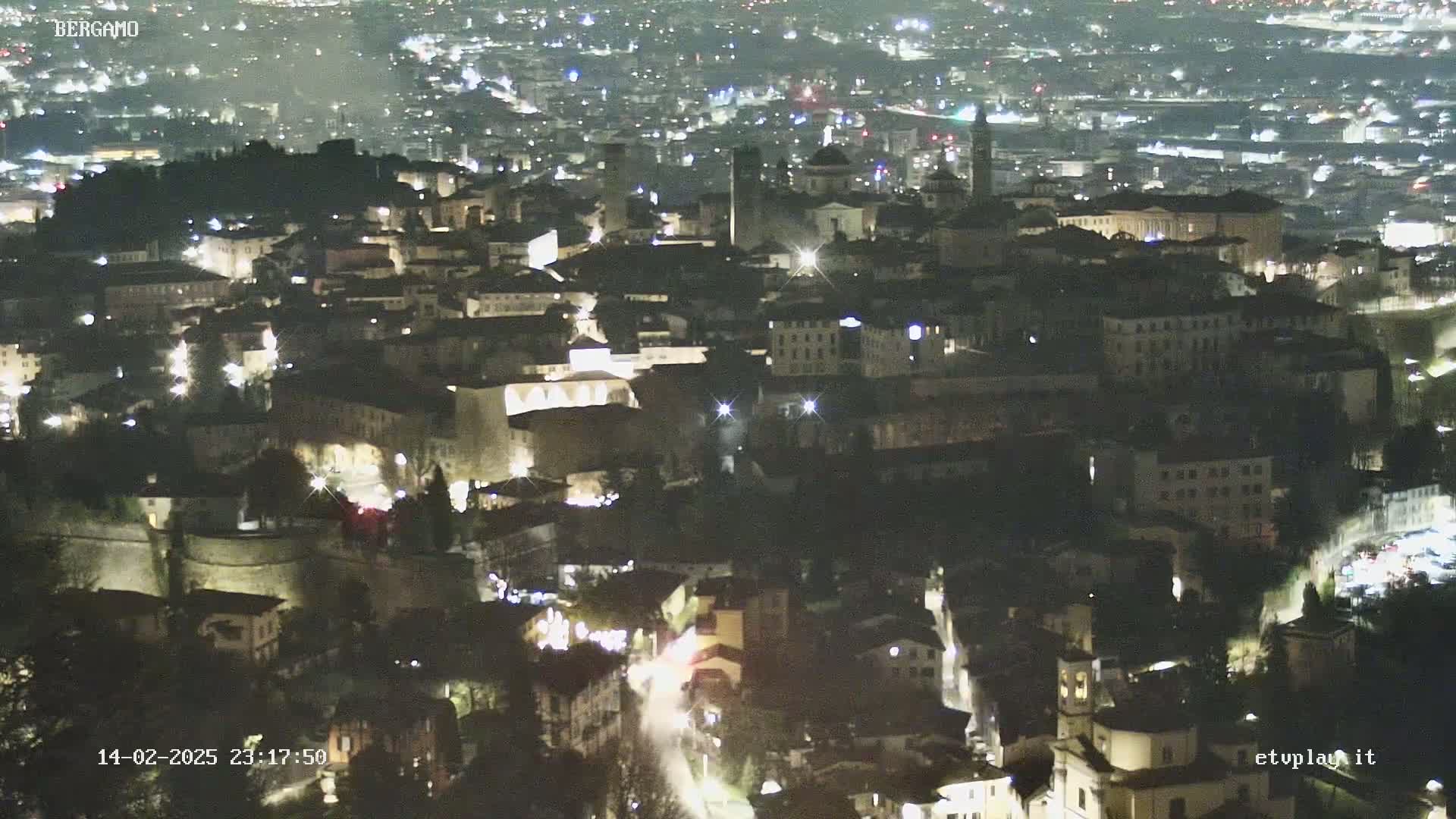 A nighttime, aerial view of a city illuminated by streetlights, showing a dense collection of buildings nestled on a hill.
