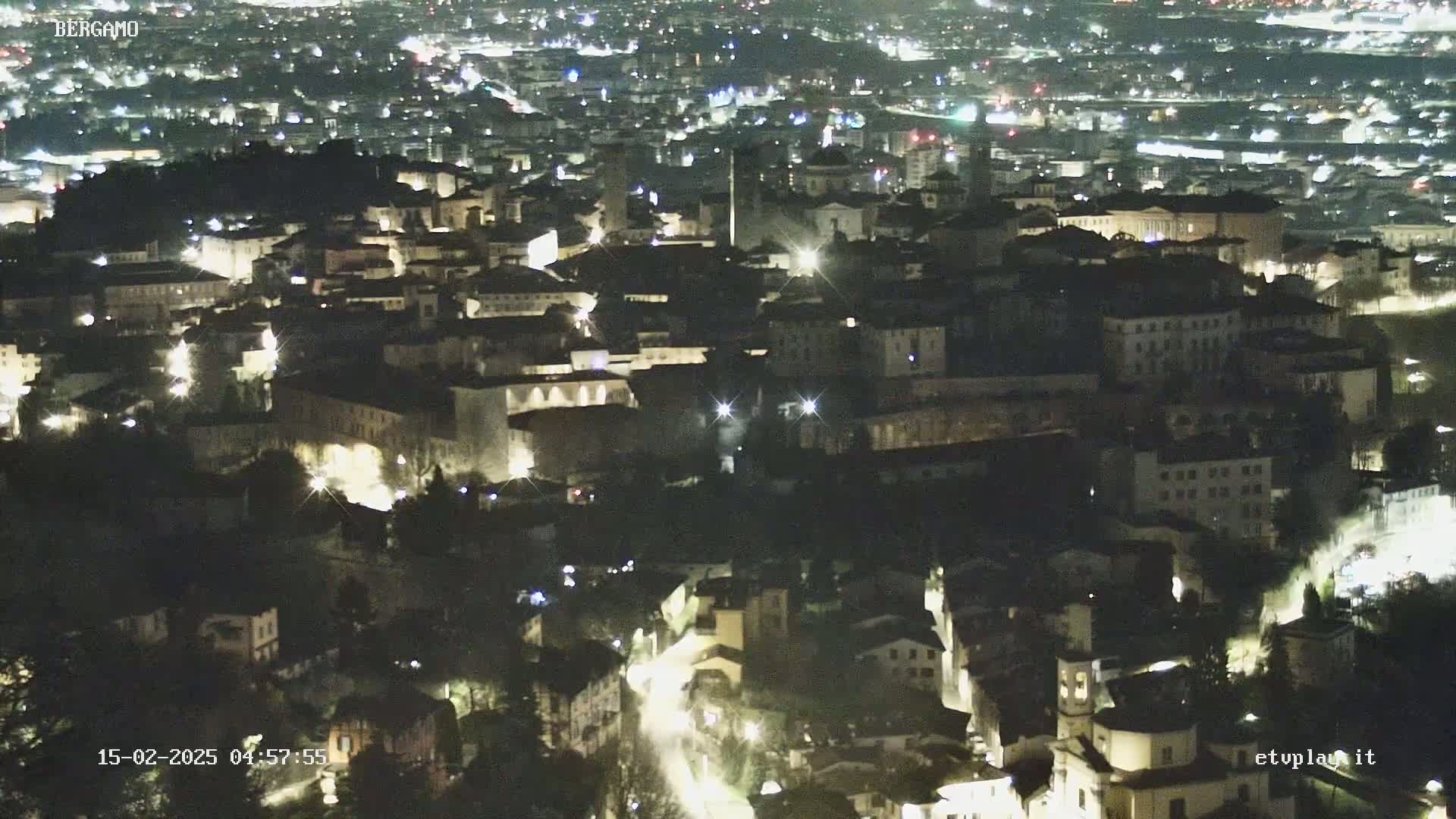 A nighttime, high-angle view of a city with many buildings illuminated by lights.
