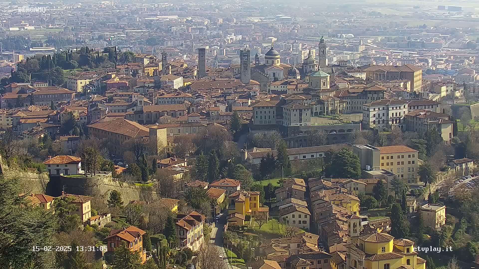 A sprawling city of terracotta-roofed buildings nestled in a valley under a sunny sky.