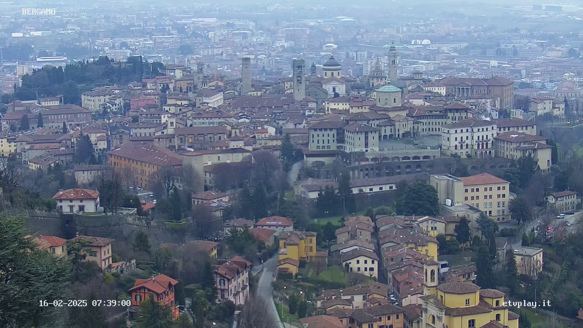 A sprawling city with numerous buildings of varying heights and styles, viewed from above on an overcast day.