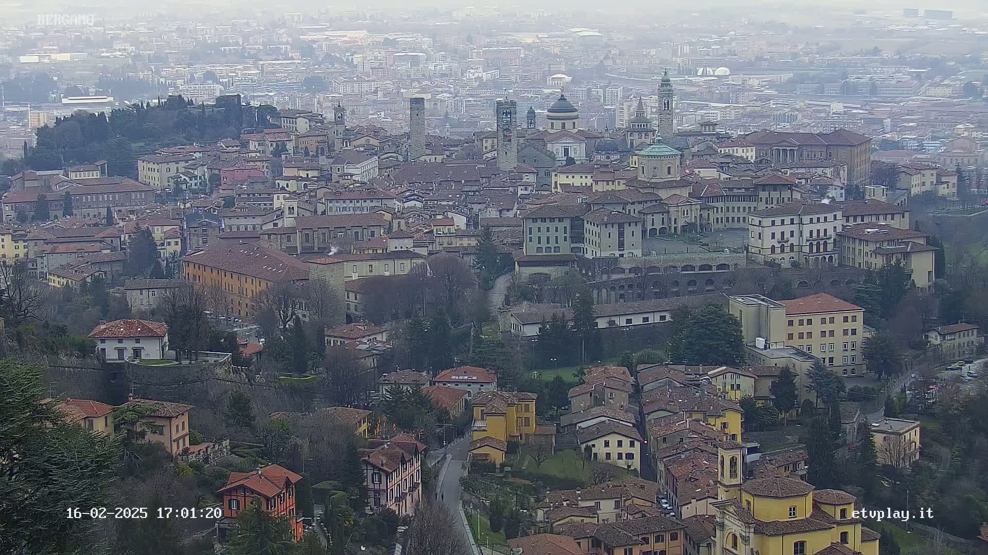 A sprawling city with numerous buildings of varying heights and architectural styles is seen on an overcast day.